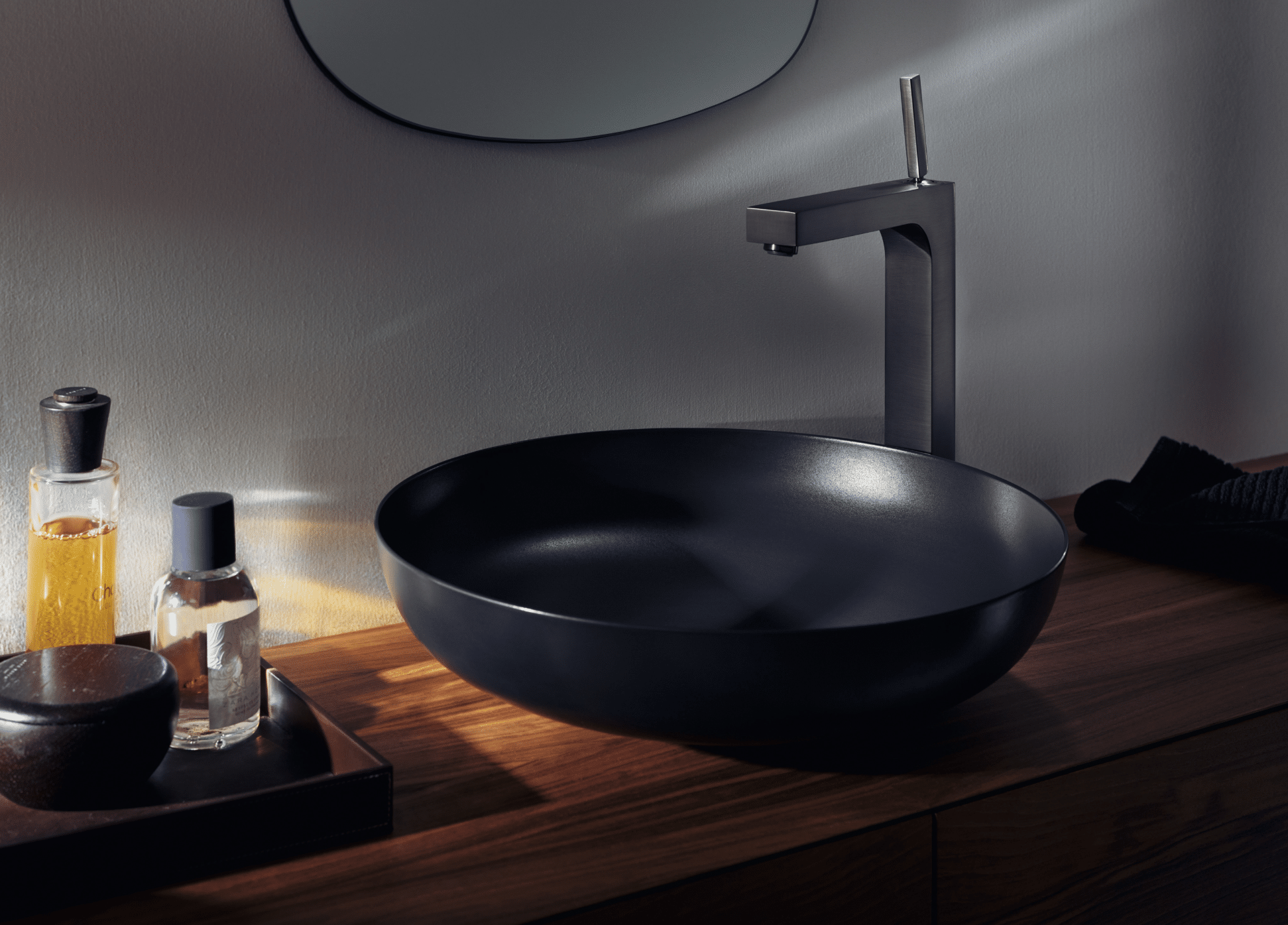 Hansgrohe zeigt eine runde, schwarze Waschschüssel mit glänzend brauner Armatur auf einem Waschtisch in Holzoptik.