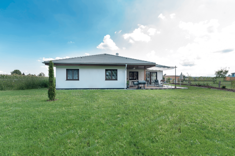 HARTL HAUS Holzindustrie zeigt einen klassische Bungalow in Fertighausbauweise mit Walmdach und überdachter Terrasse.