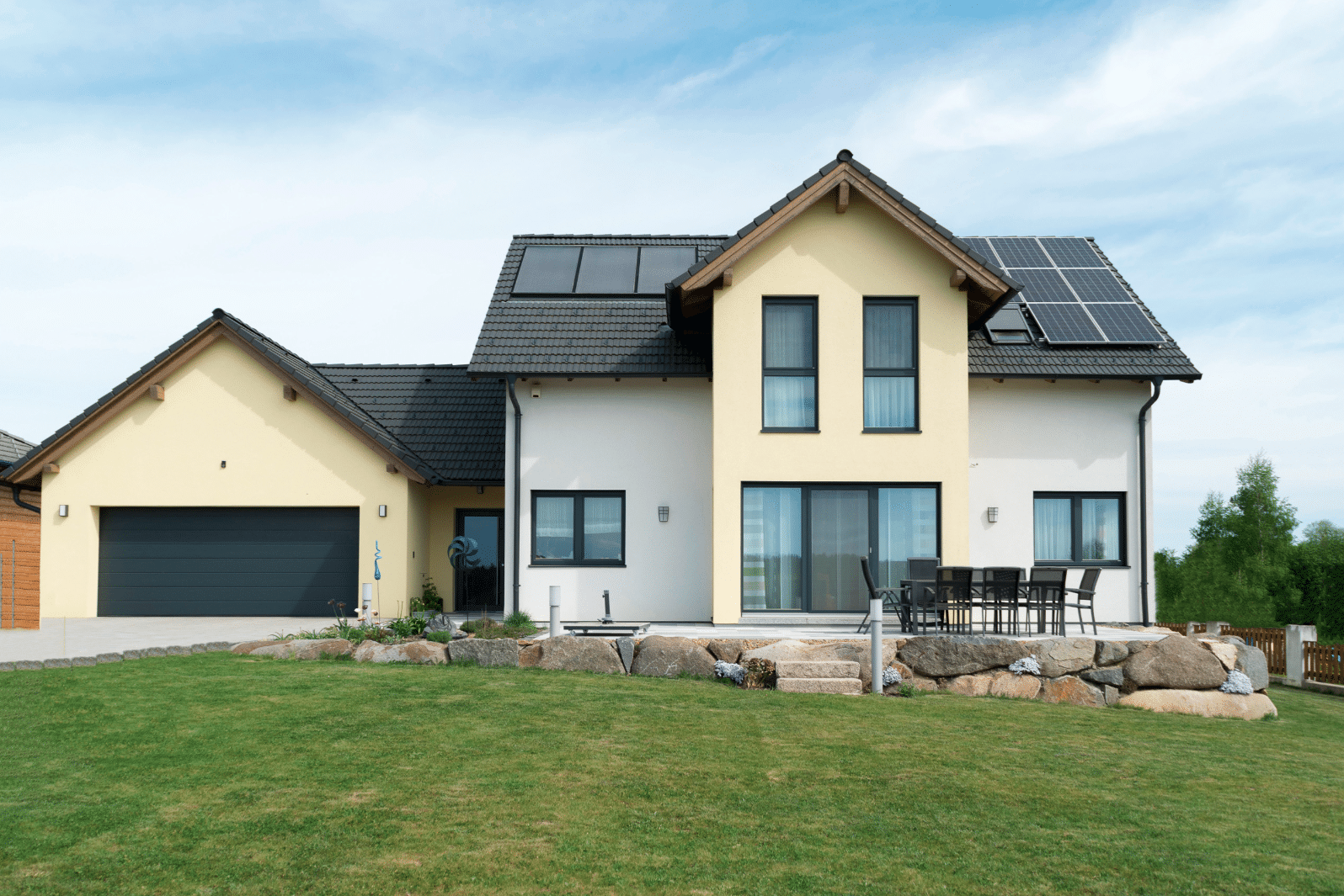 HARTL HAUS Holzindustrie zeigt ein modernes Fertighaus mit Zwerchdach und Solarkollektoren, Doppelgarage sowie Terrasse.