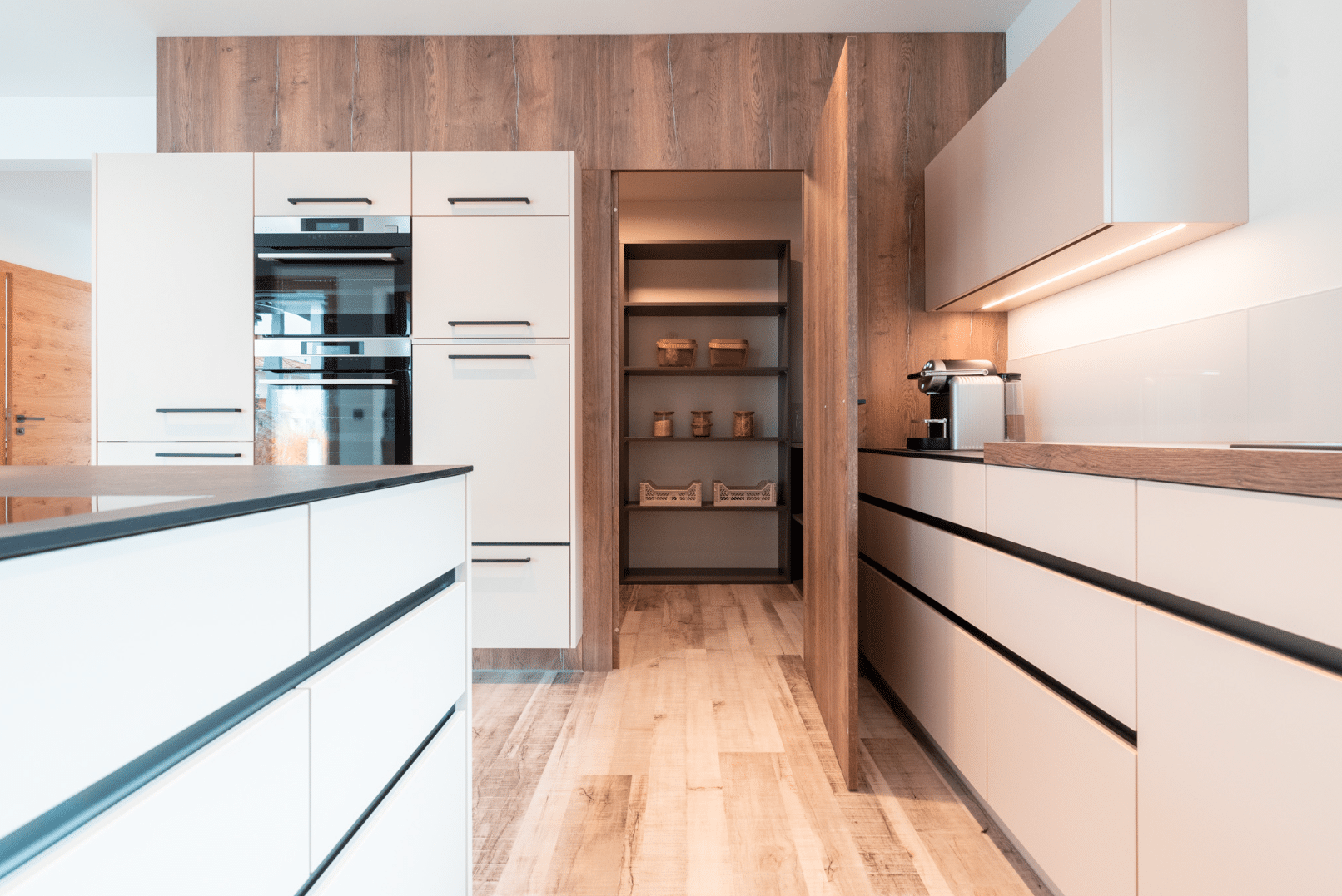 Hartl Haus zeigt eine weiße Küche mit einem Abstellraum praktisch versteckt hinter einer Holzverkleidung.