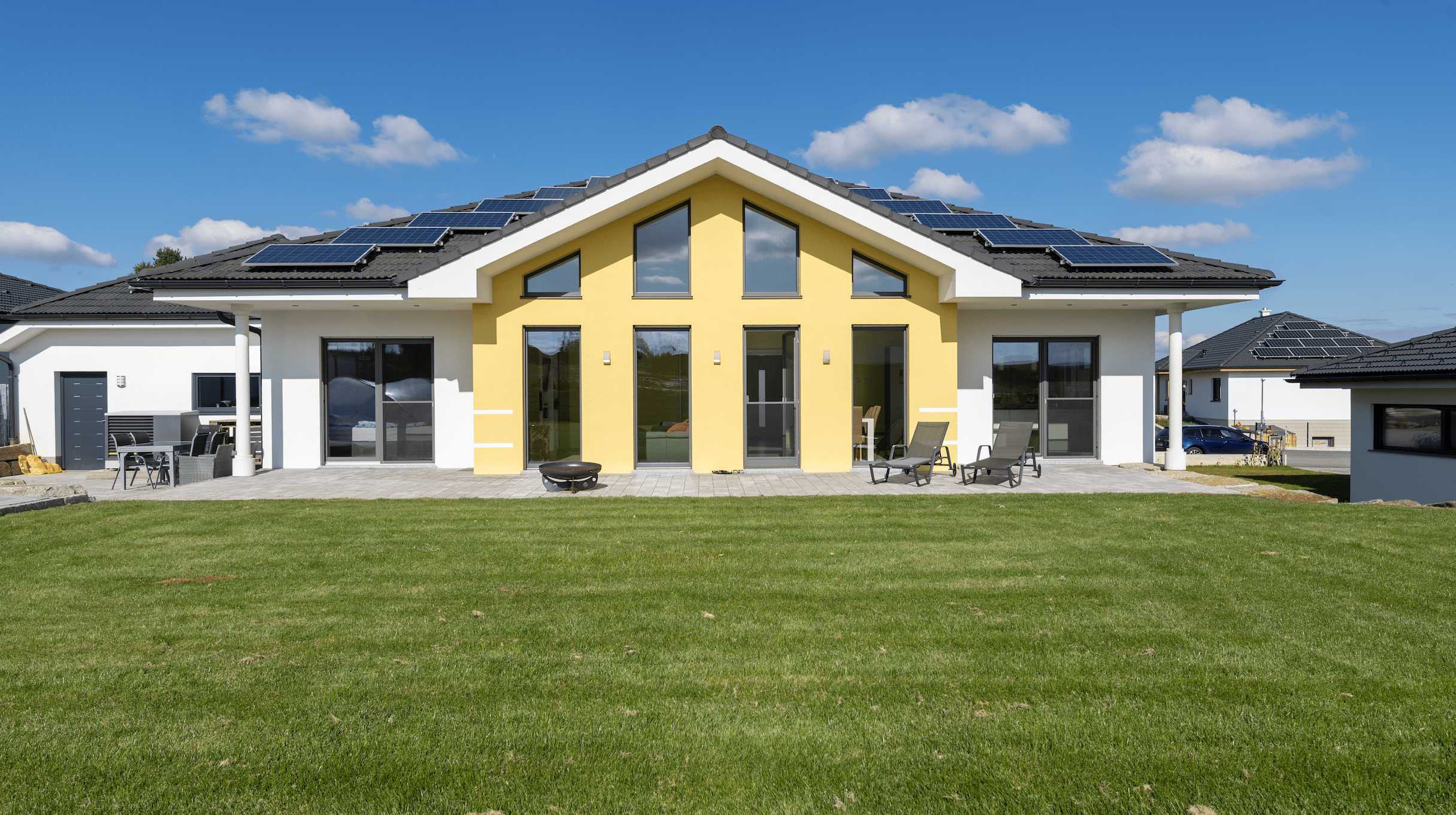 Hartl Haus zeigt ein weiß-gelbes Einfamilienhaus mit enormen Garten, Terrasse und Photovoltaikanlage am Dach.