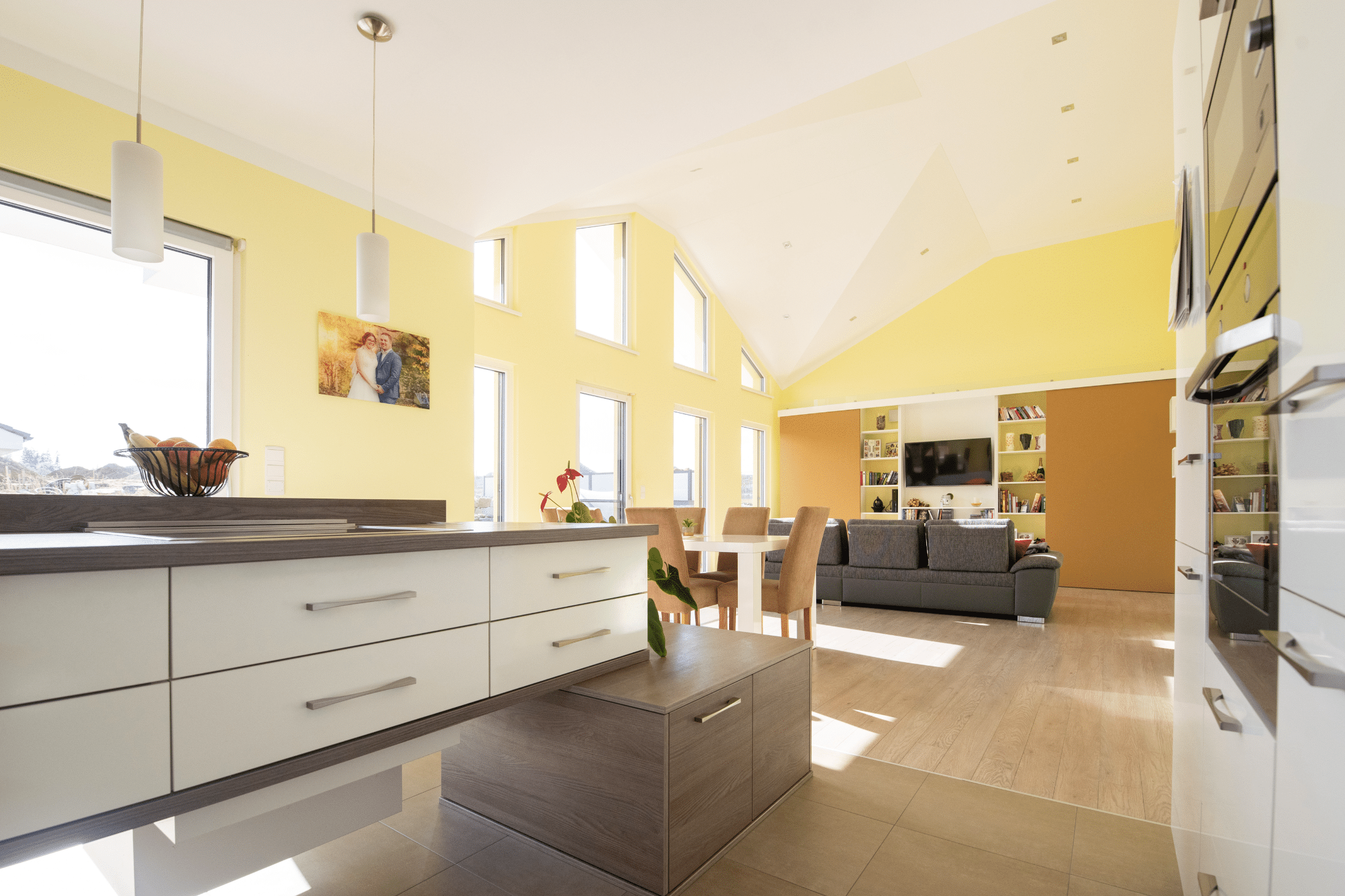 Hartl Haus zeigt eine sher moderne, weiße Küche mit Kästen aus Holz,einer Pflanze und gelben Wänden.