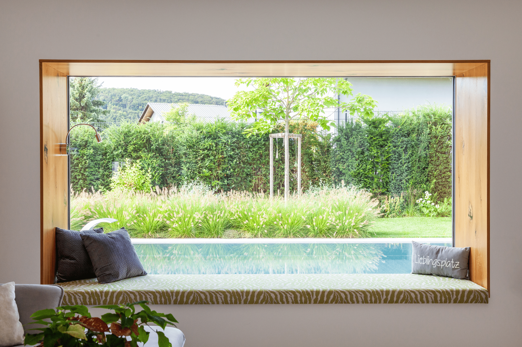 Hartl Haus zeigt ein Fenster, welches in den Garten und den Pool blickt, mit kleiner Sitzbank davor.