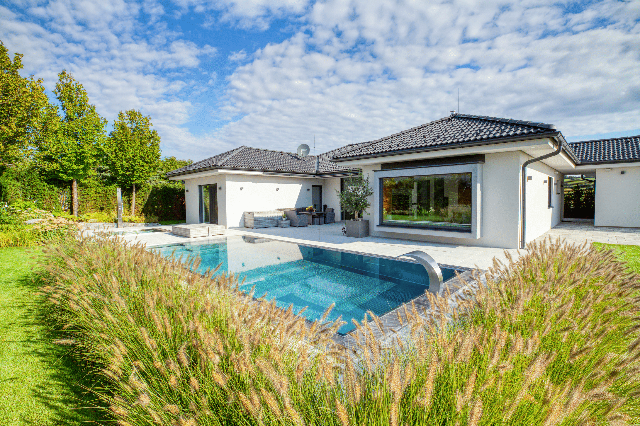 Hartl Haus zeigt einen weißen Bungalow mit schwarzem Walmdach und einem rechteckigen Pool auf der Terrasse.