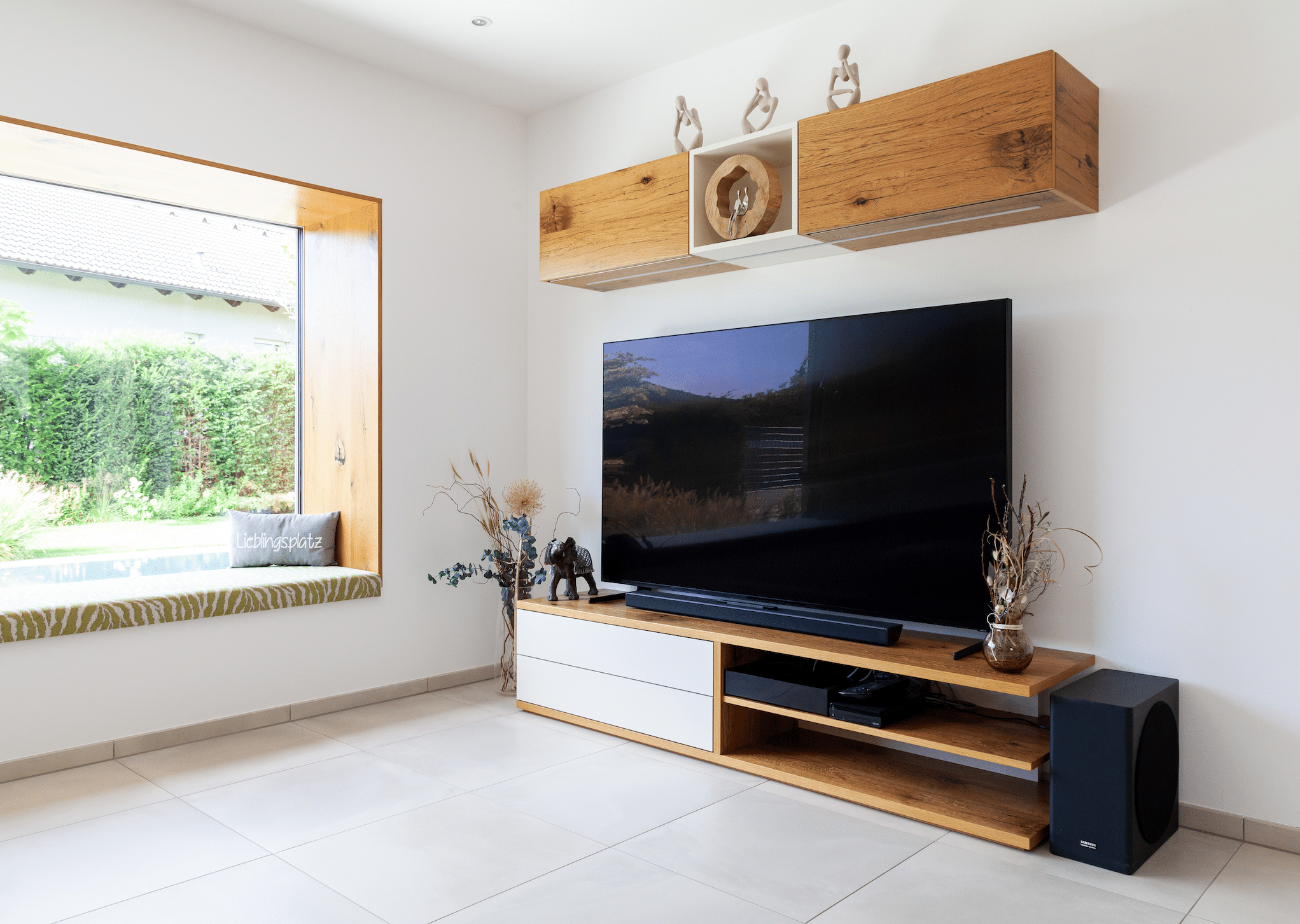 Hartl Haus zeigt eine Wohnwand aus Holz mit weißen Laden, einem Fernseher und Holzdekoration.