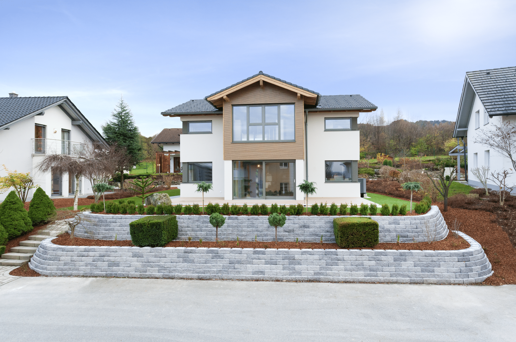Hartl Haus zeigt ein helles Einfamilienhaus mit Holzverkleidung, Terrasse und gepflegtem Vorgarten mit Stufen und Zugang zum Haus aus Steinplatten.