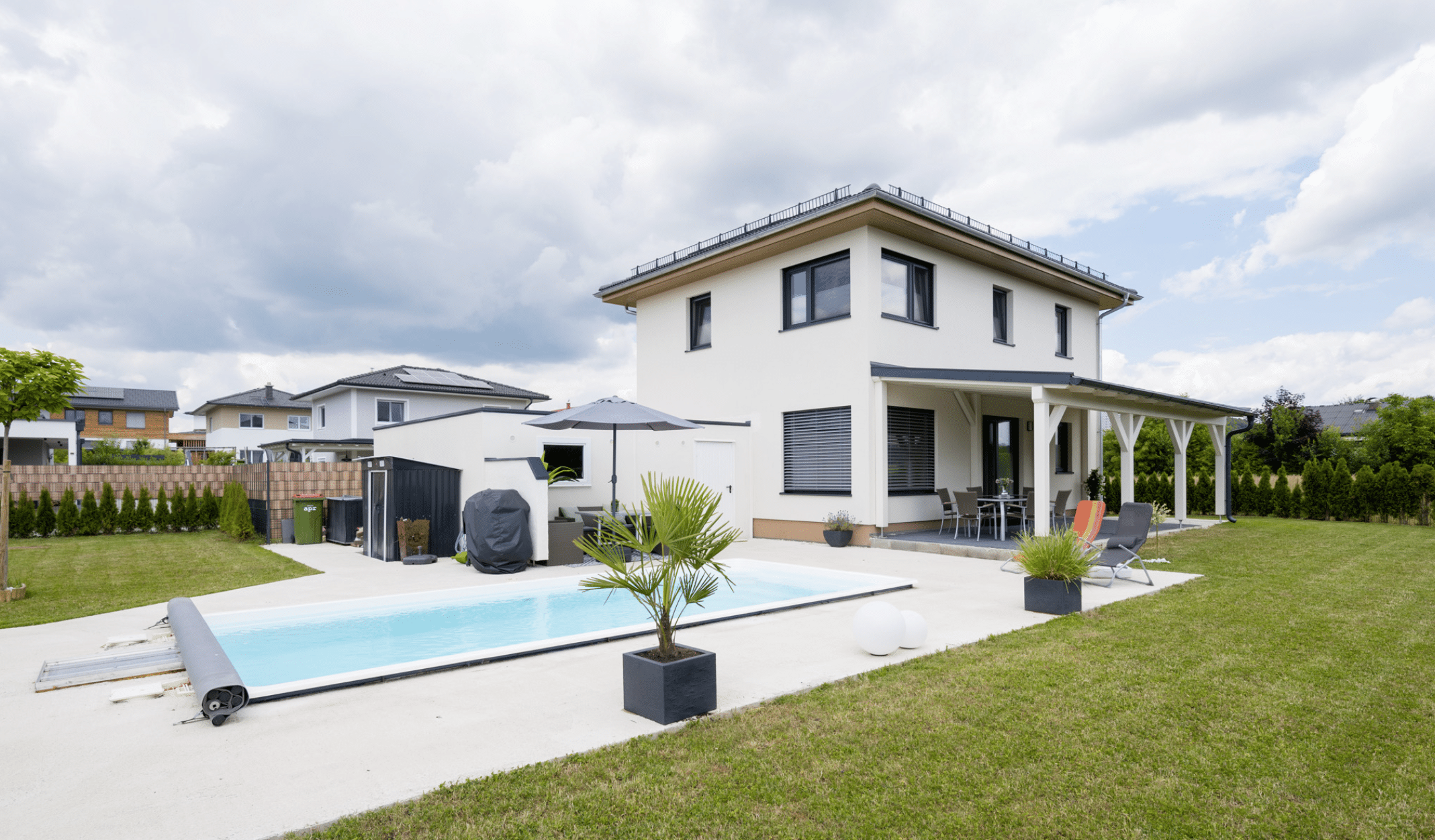 HARTL HAUS zeigt ein zweistöckiges, modernes Einfamilienhaus in der Farbe weiß, mit Pool, großem Garten und überdachter Terrasse.