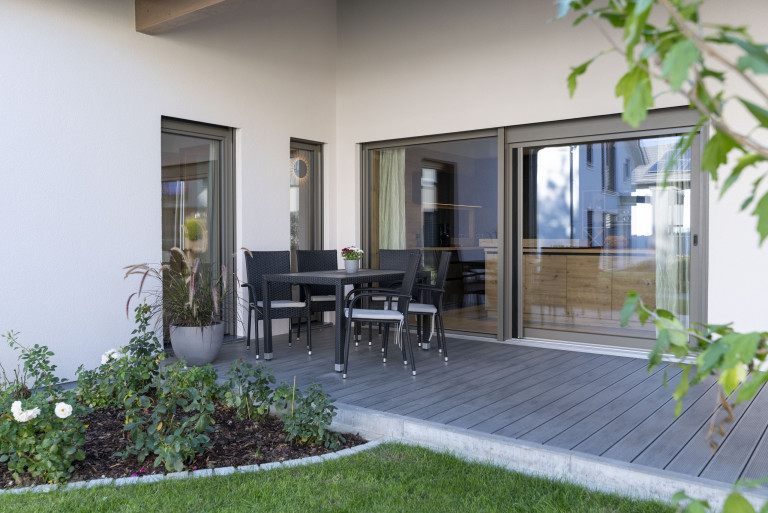 Hartl Haus zeigt Terrasse mit dunklem Holzboden vor einer großen Glasschiebetür.