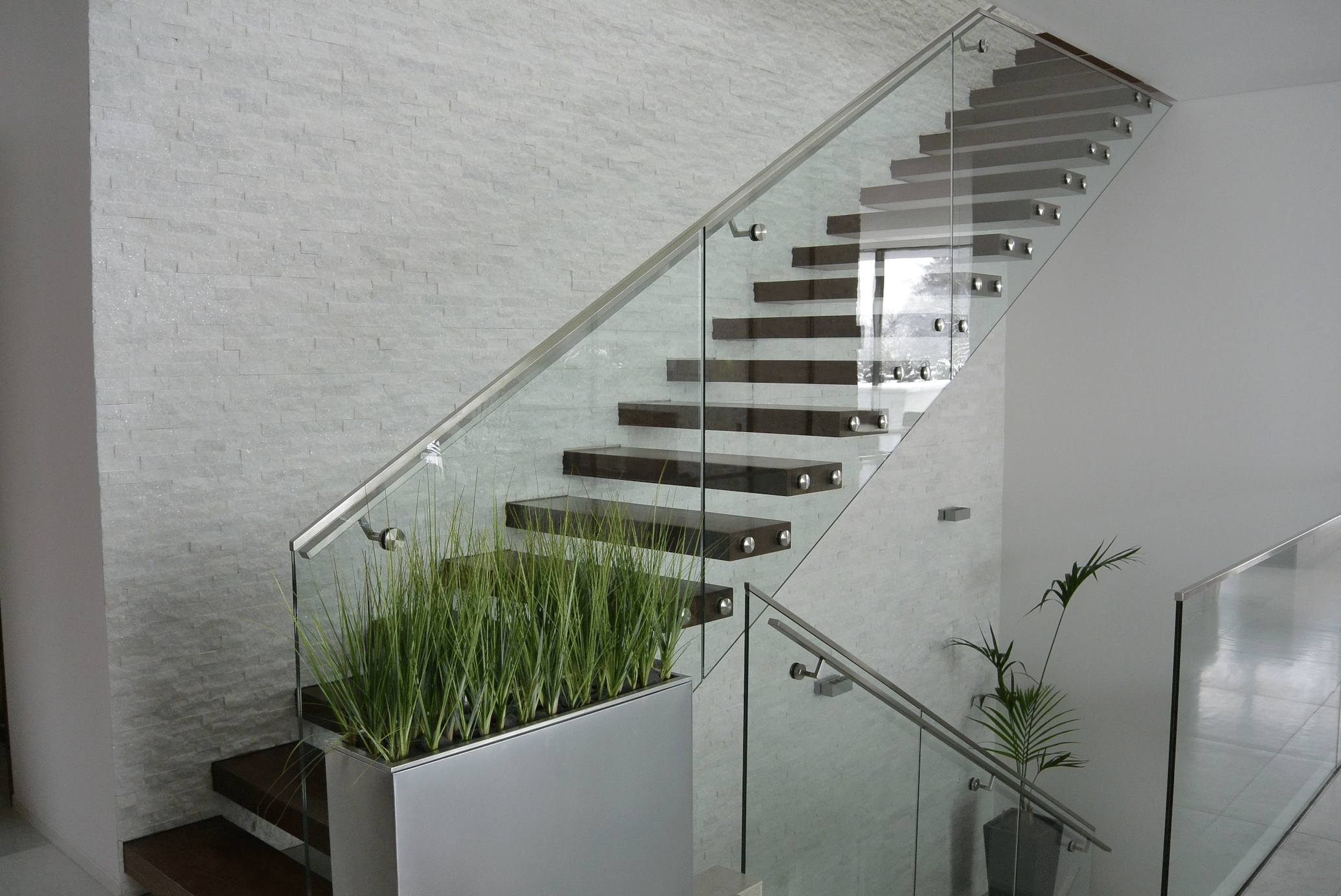 Hausjell zeigt ein modernes Stiegenhaus mit Pflanzen und Holztreppen mit einem Geländer aus Glas und silberner Haltestange.
