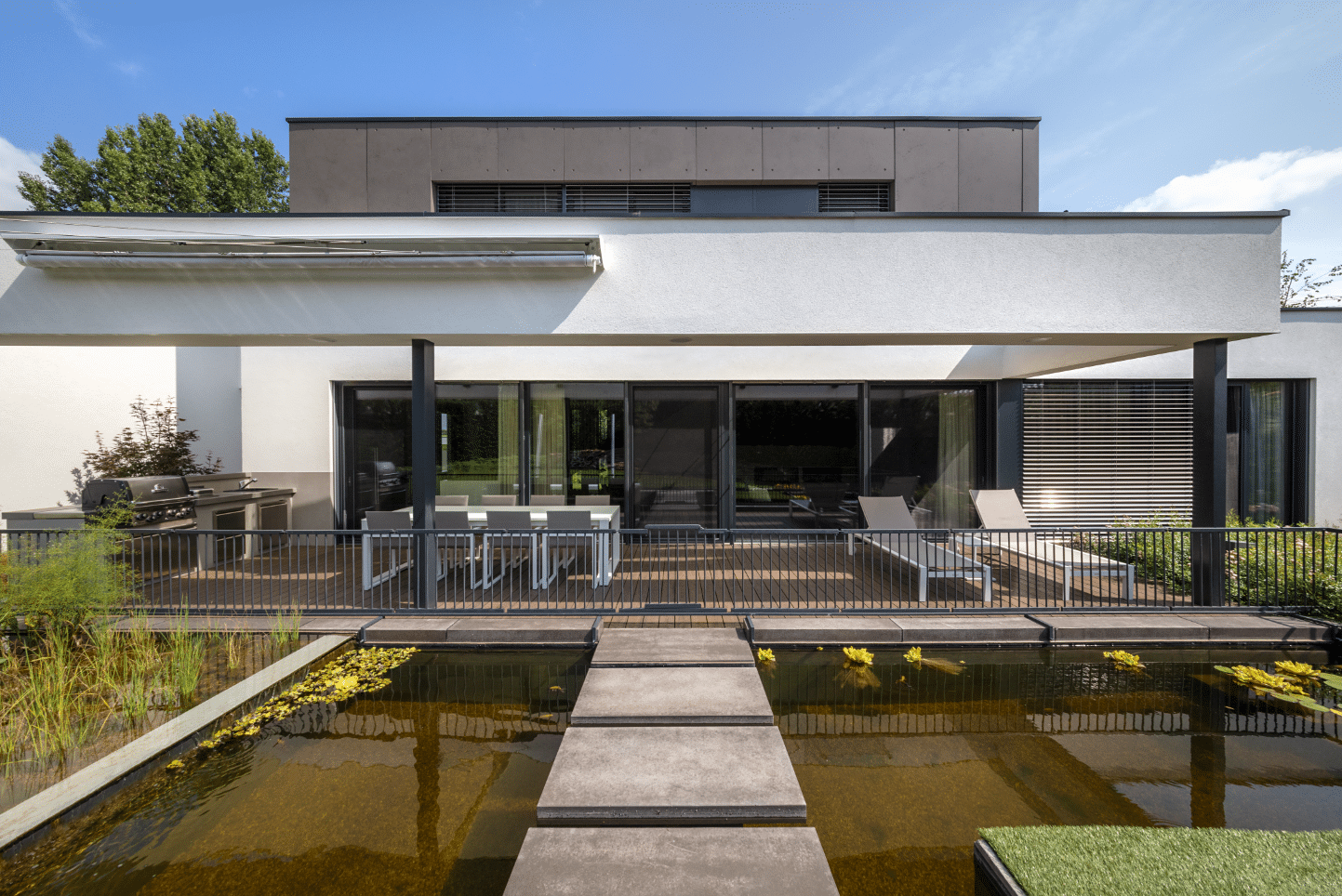Modernes Haus im Bauhaus-Stil mit Flachdach, Teich, Steg, Terrasse und deckenhohen Fenstern sowie Terrassentüren von Internorm.