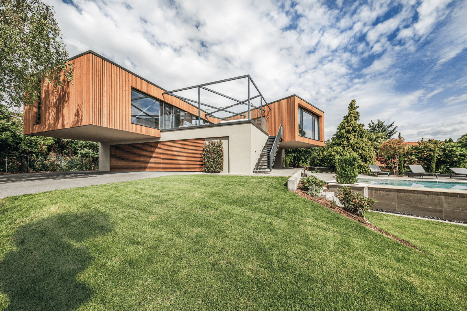 Internorm zeigt ein Architektenhaus mit Holzfassade, Balkon und Treppen zum Garten mit Pool.