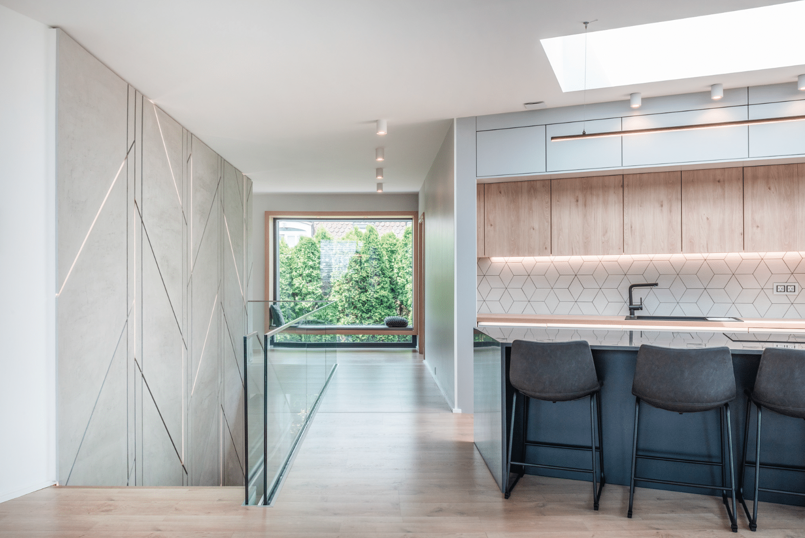 Internorm zeigt eine offene Küche neben einem Treppenabgang mit langem Flur zu einem großen Fenster mit Sitzgelegenheit.