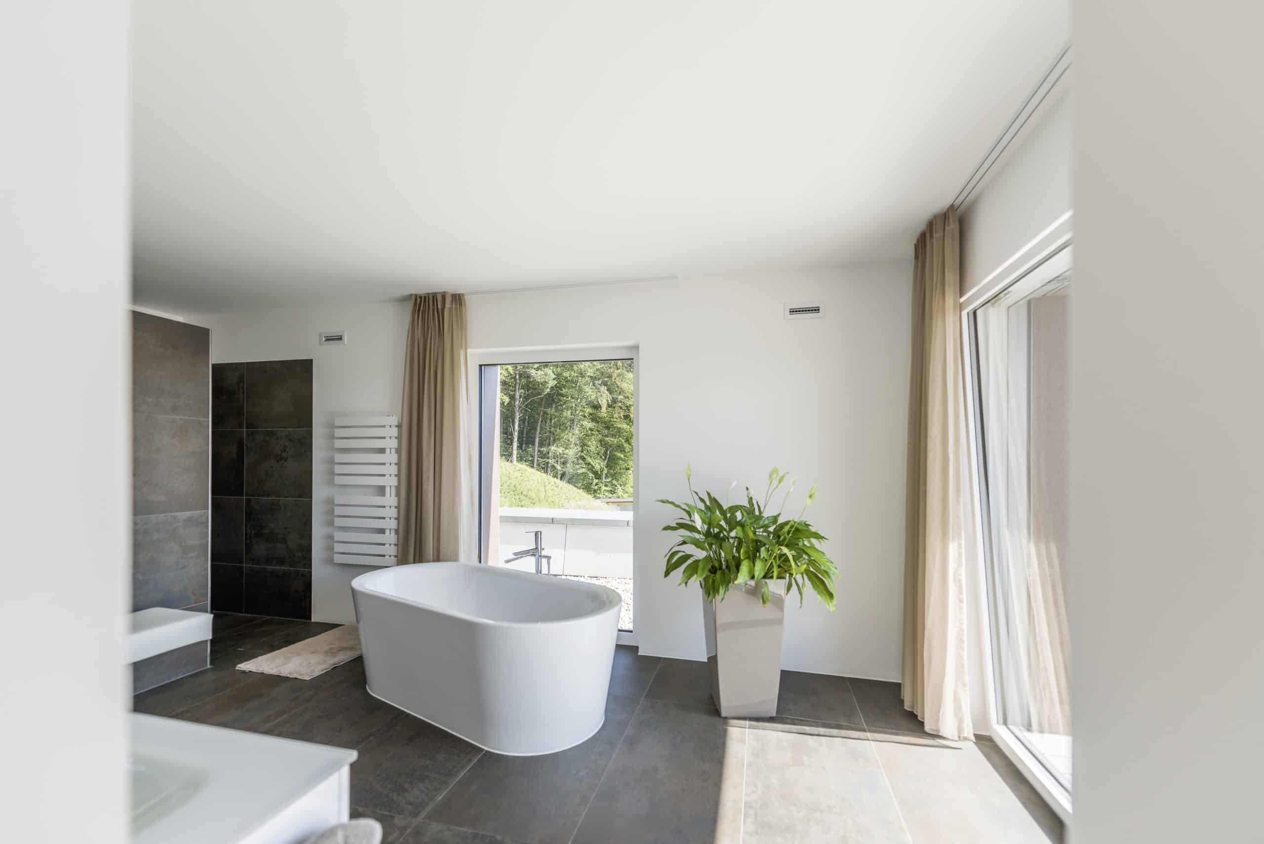 Internorm zeigt ein Badezimmer mit großem Fenster, freistehender Badewanne und beige Vorhänge.