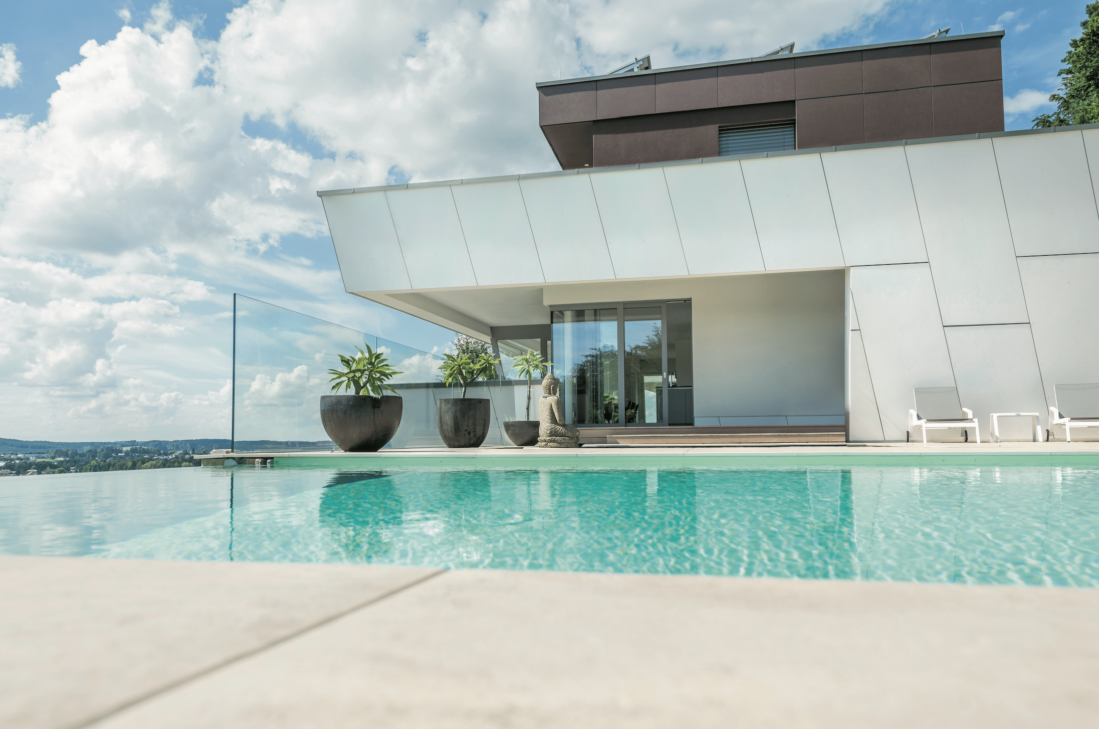 Internorm zeigt eine Außenanlage mit Pool, weißem Haus und Glasfronten um dem Pool einen Infintiylook zu verleihen.