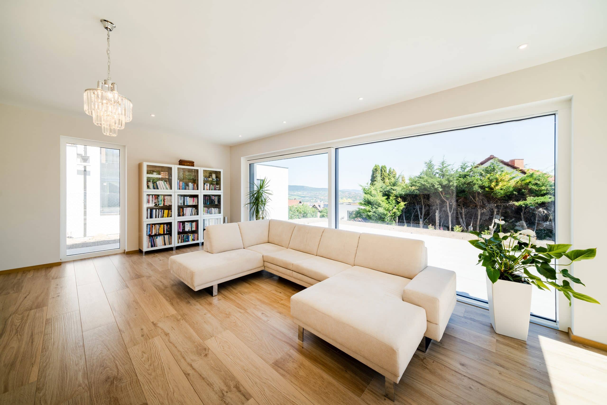 Internorm zeigt eine vollverglaste Wand eines Wohnzimmers in dem eine beige Couch und ein Bücherregal stehen.