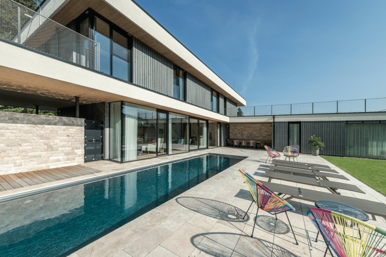 Großflächige Terrasse mit länglichem Pool und mit großflächigen Bodenfliesen und großen Fensterflächen und Glasschiebetür von Internorm, die auf die Terrasse führen.