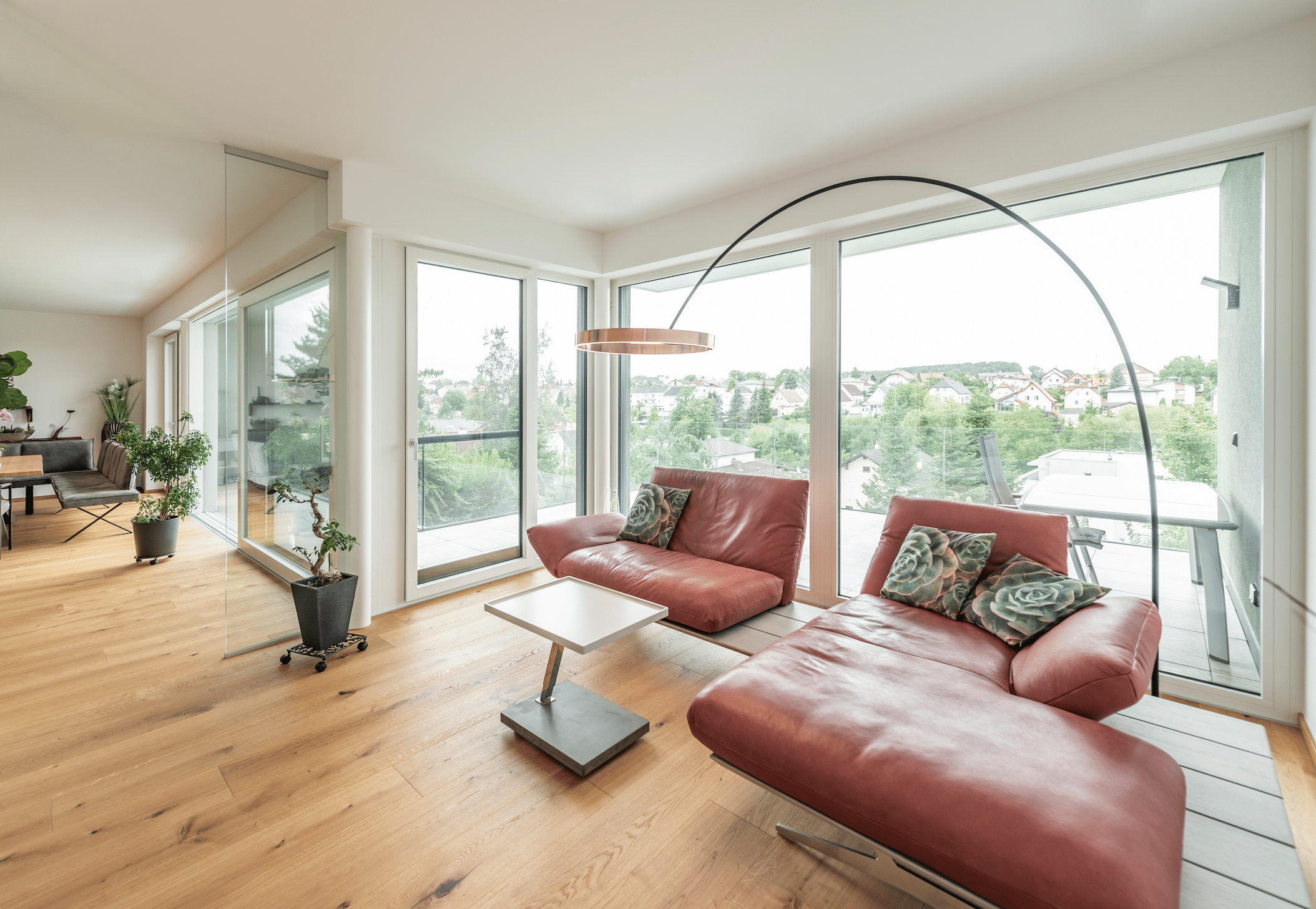 Helles Wohnzimmer mit Holzboden und großen Fensterfront mit Glasschiebetür und Glastür von Internorm, die auf den Balken führen.