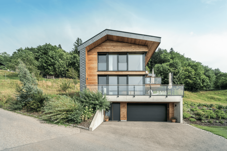 Internorm zeigt ein Einfamilienhaus in schwarz mit Holzakzenten, einem großen Balkon und Glasfronten, mit schwarzer Haustüre und Garagentor.