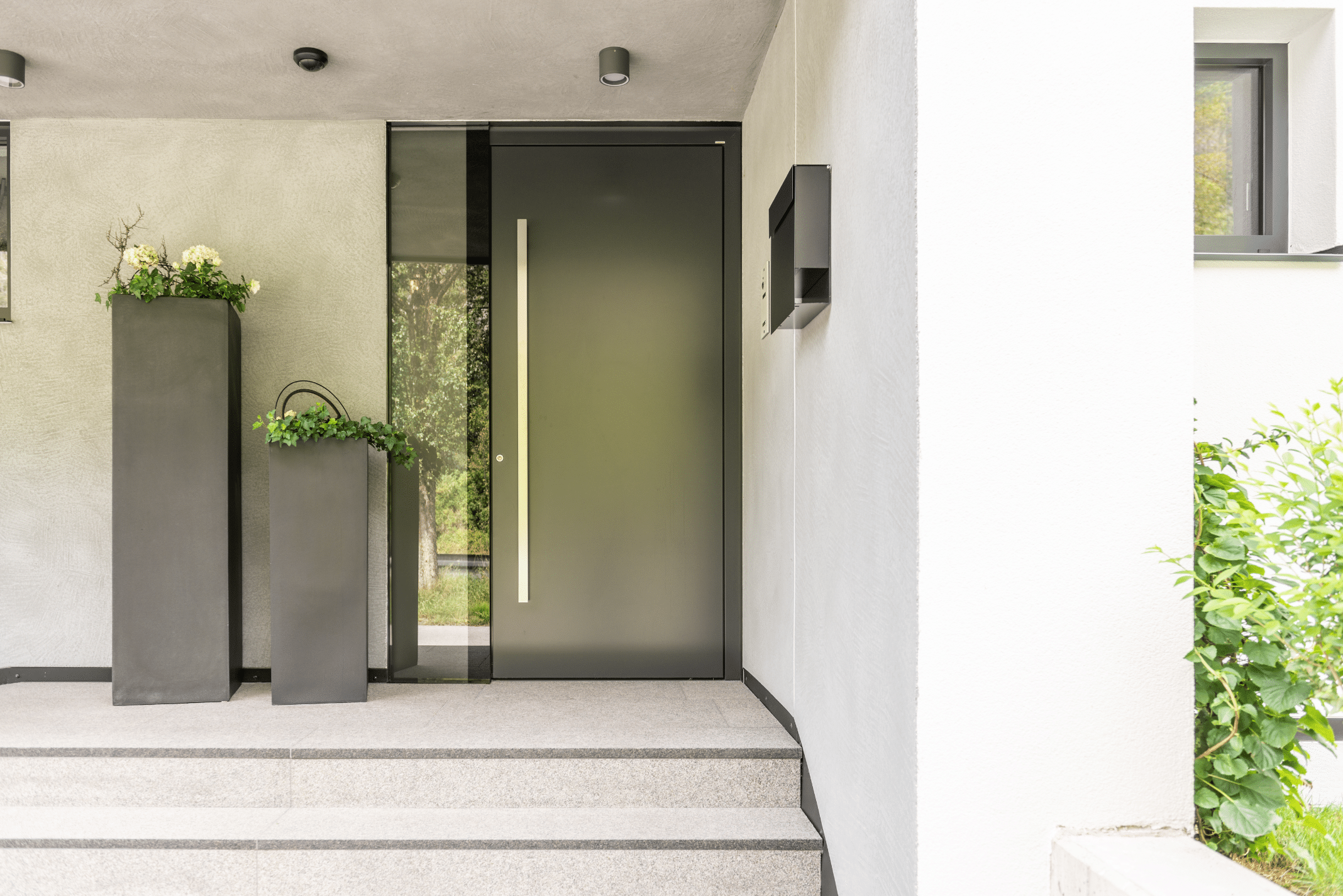Internorm zeigt einen Hauseingang mit einer schwarzen Haustüre mit silbernem Griff und Fenster mit großen, eckigen Blumentöpfen daneben.