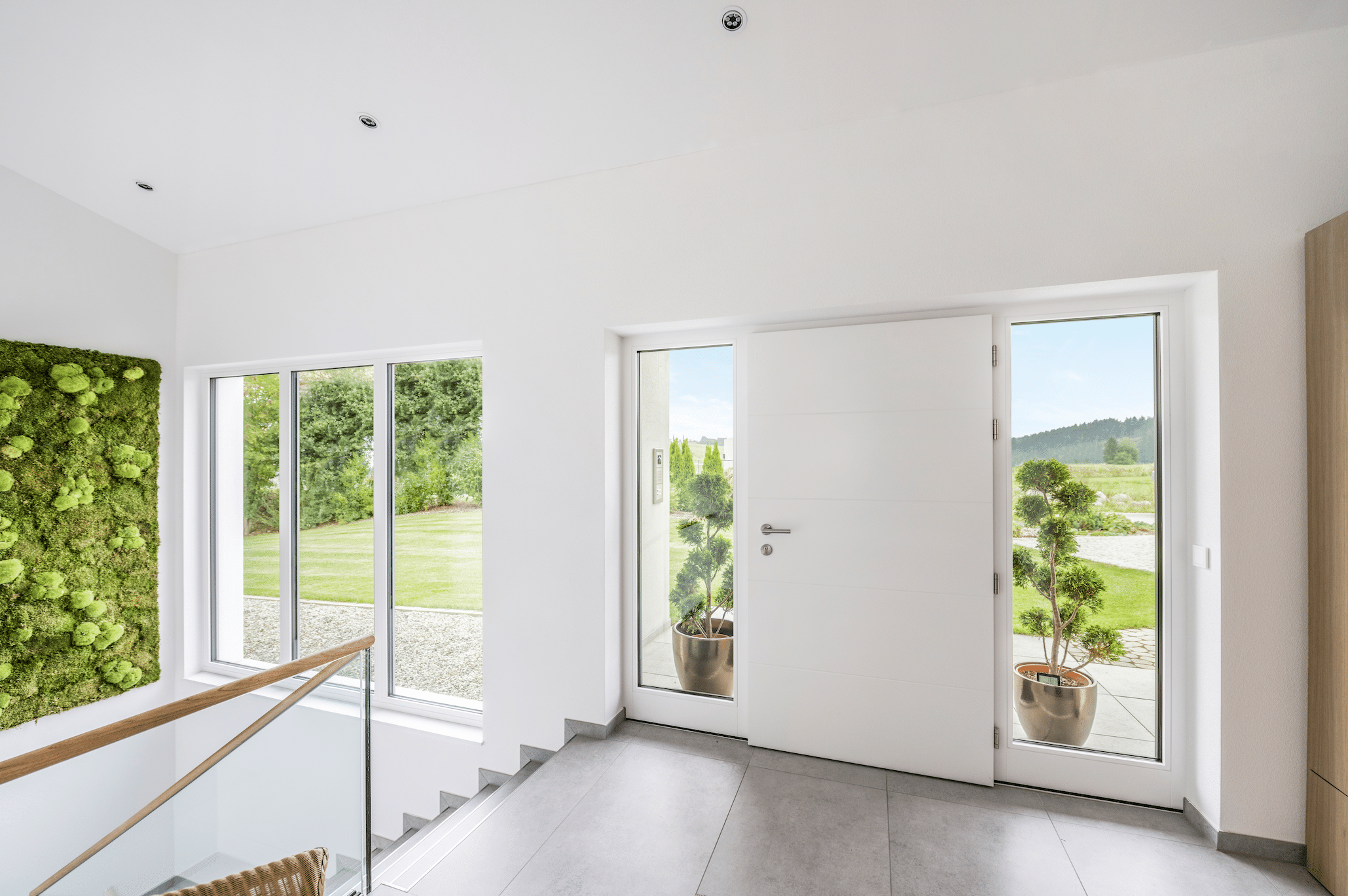 Internorm zeigt den Eingangsbereich eines Einfamilienhauses mit einer weissen Haustüre, großen Sichtfenstern einer Glaswand und mit Treppen die in das Untergeschoss führen.