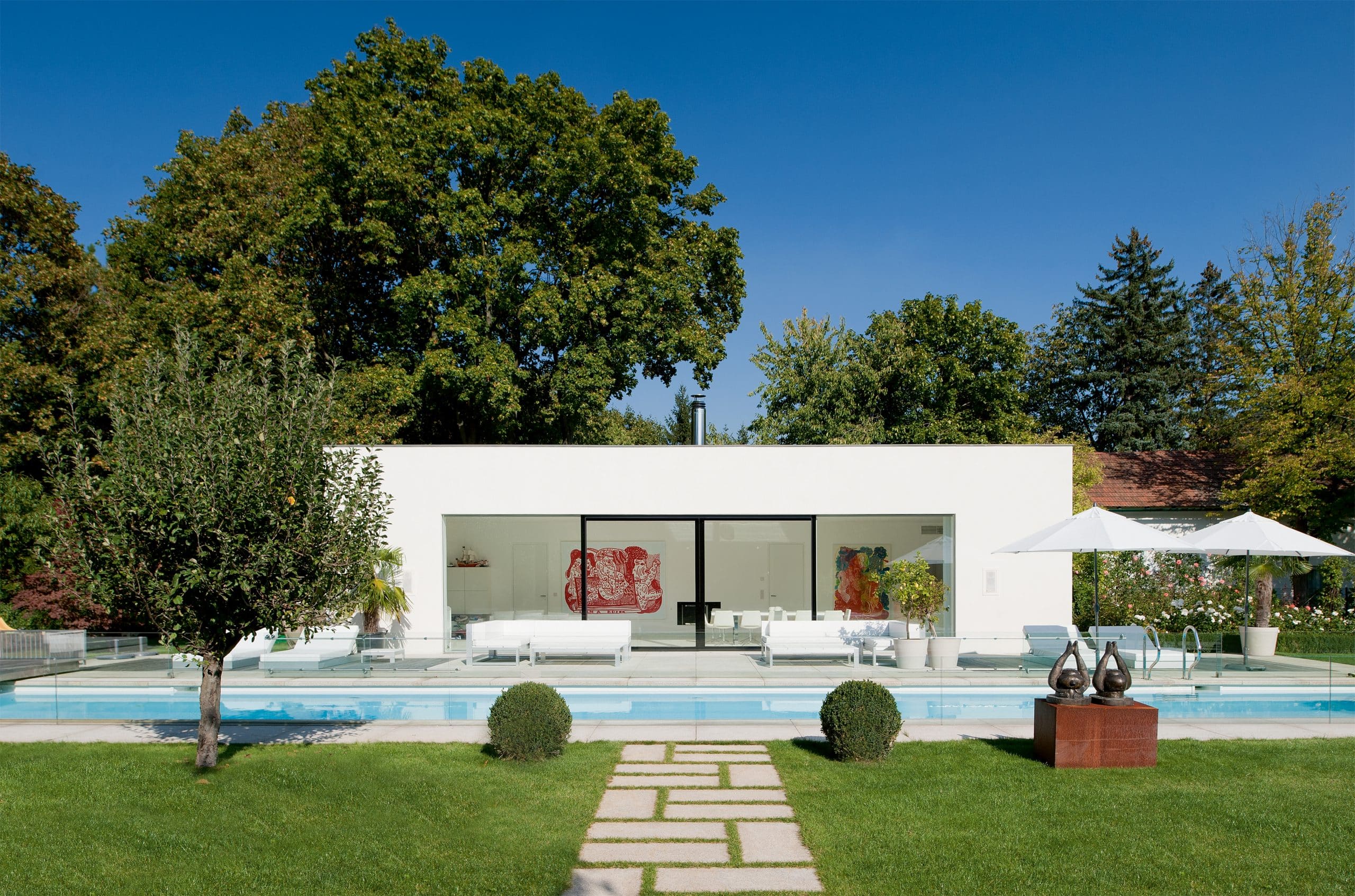 Modernes, exklusives Poolhaus mit Flachdach, breitem Ganzglas-Schiebessystem von Josko und großem Pool und Lounge-Möbel auf der Terrasse.