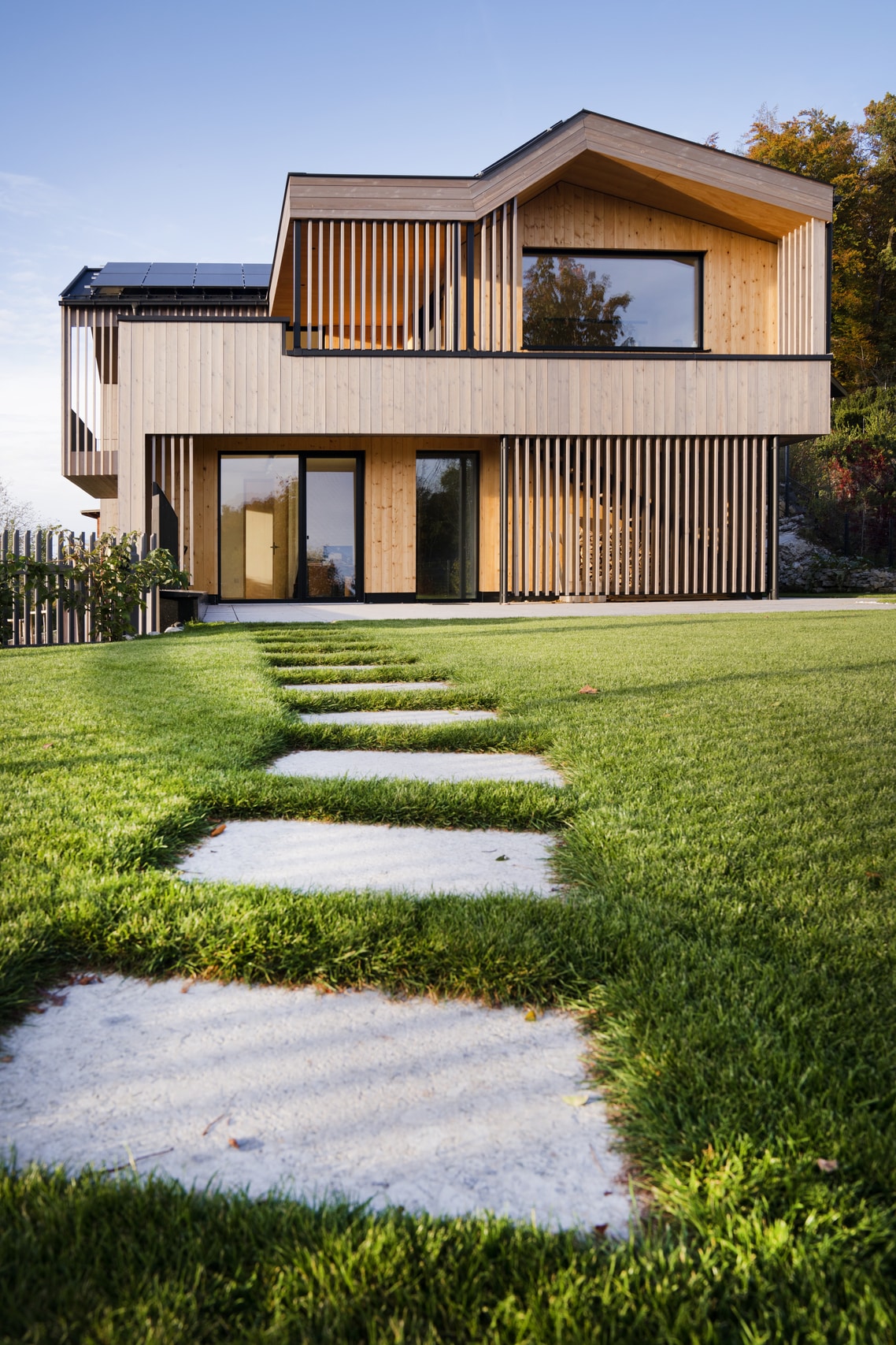 Modernes Holzhaus mit Garten, großem fixverglastem Fenster und Glastüre mit schwarzem Rahmen von Josko.