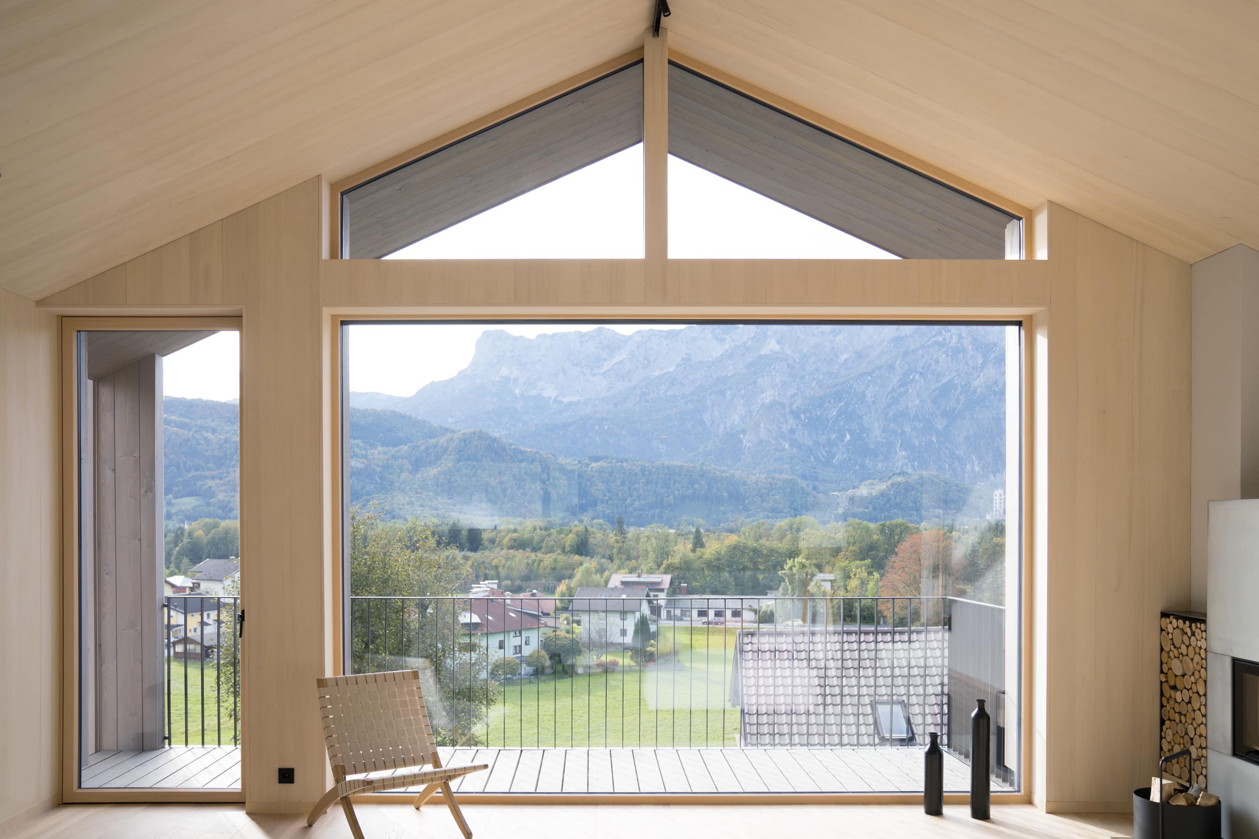 Heller Wohnbereich mit Kamin, raumhoher Glasfront, Glastüre und Giebelfenster von Josko in einem Holzhaus.