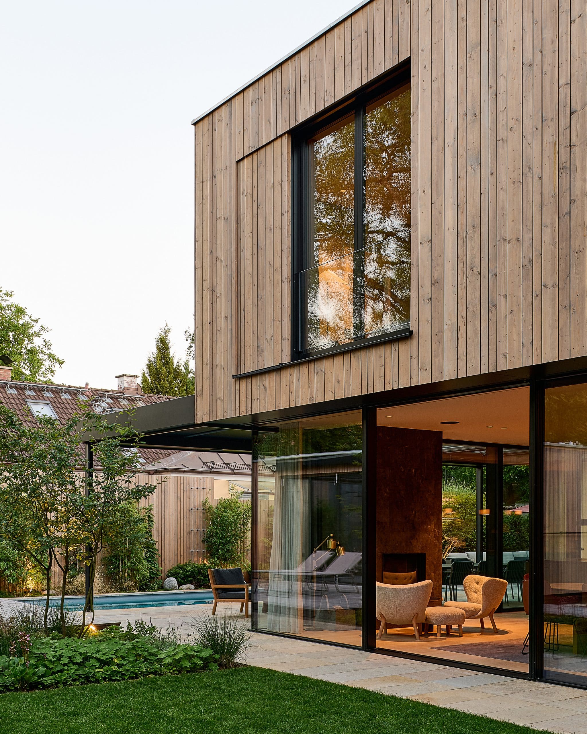 Modernes Flachdach-Holzhaus mit Ganzglassystem und Glasschiebetüre mit schwarzem Rahmen von Josko mit Blick in den Wohnbereich.