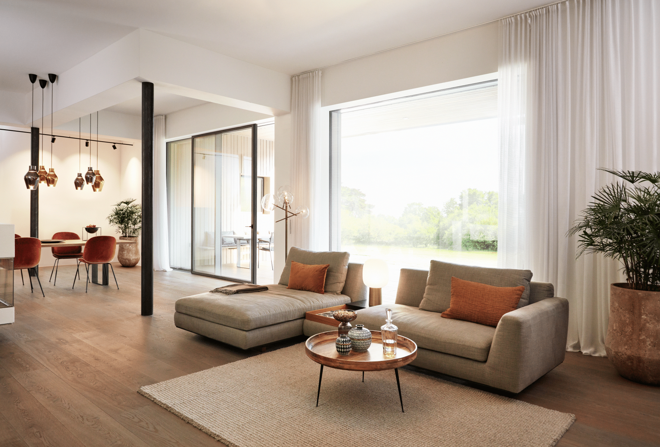 Wohnzimmer mit Holzboden, Wohnlandschaft und deckenhohen Fenstern sowie Glasschiebetüren mit schwarzem Rahmen aus der Serie ONE by Josko.