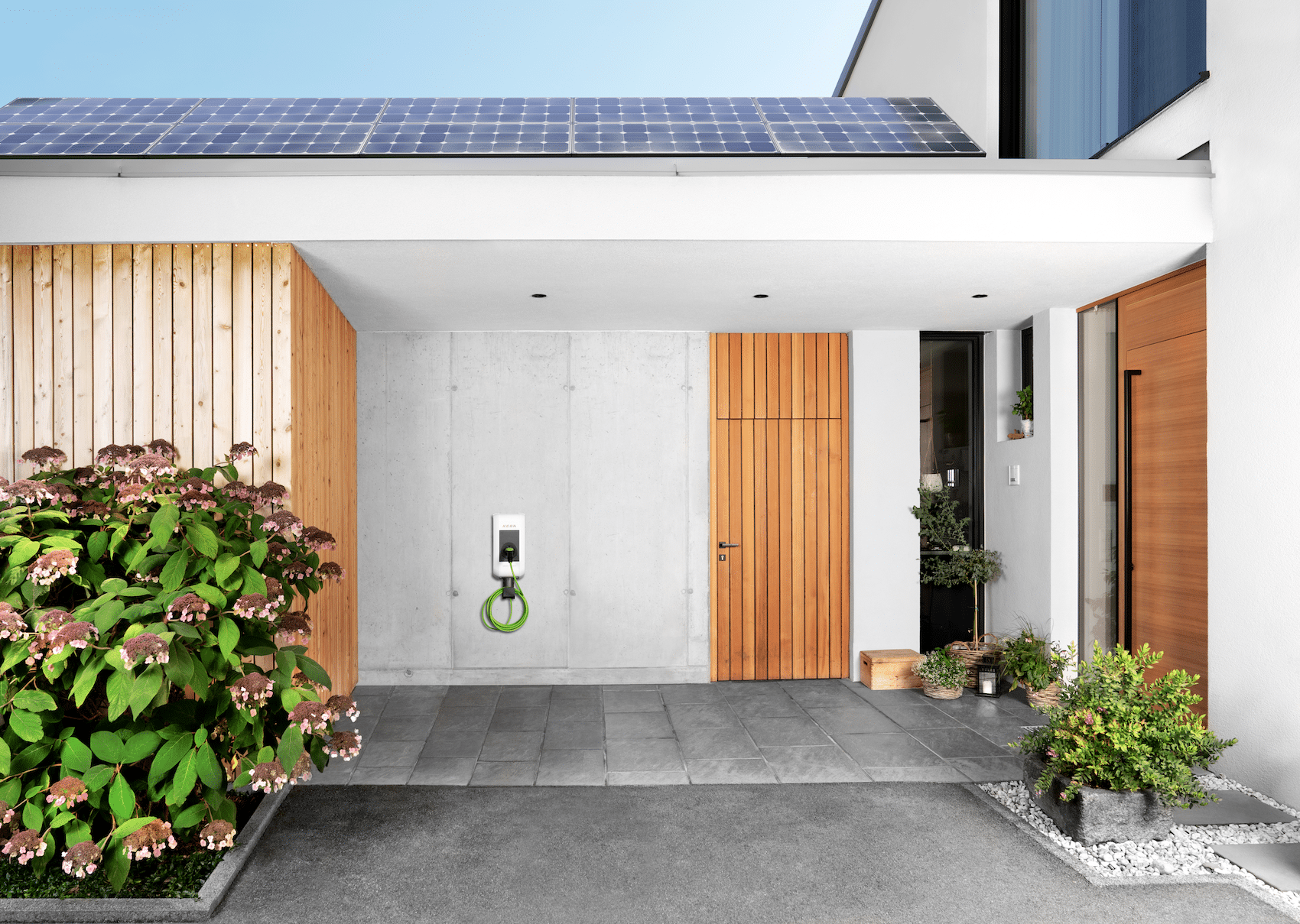 KEBA zeigt eine Wallbox-Lösung für Elektroautos, mit wenig Platzbedarf, wie in diesem Eingangsbereich mit einer Holztüre und einer Photovoltaikanlage auf dem Dach.