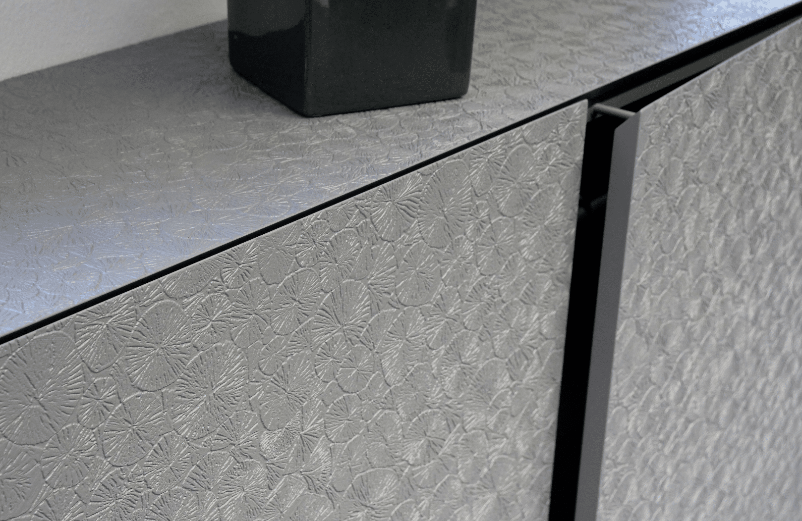 Die moderne Lasertechnik von Keplinger ermöglicht neue Wege bei der Gestaltung von Küchenfronten, in diesem Fall dunkles Holz mit Blattmuster, silber glänzend.