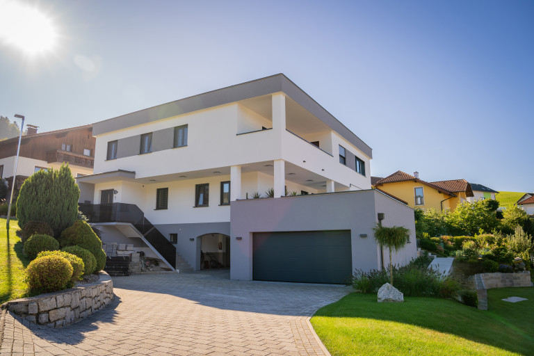 Mehrstöckiges Haus mit dunklem Stiegengeländer aus Glas, Flachdach, überdachtem Balkon und Garage mit Dachbegrünung von B. Kern Baugesellschaft.