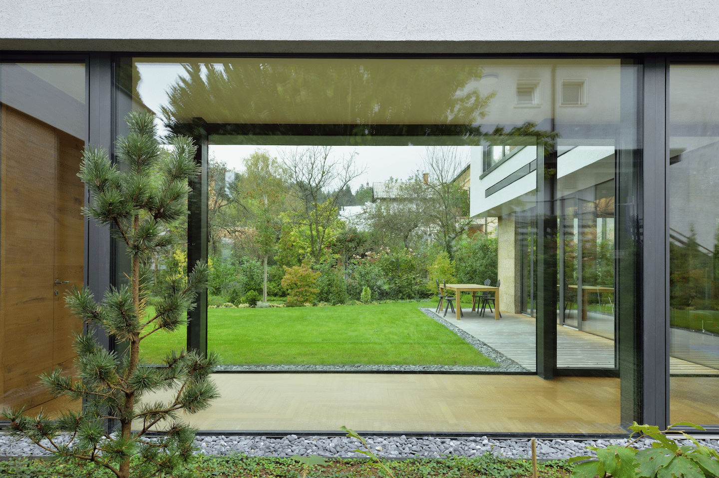 Schmaler Durchgang mit beidseitiger, deckenhoher M SORA Verglasung und M SORA Glasschiebetür zum Garten hin.