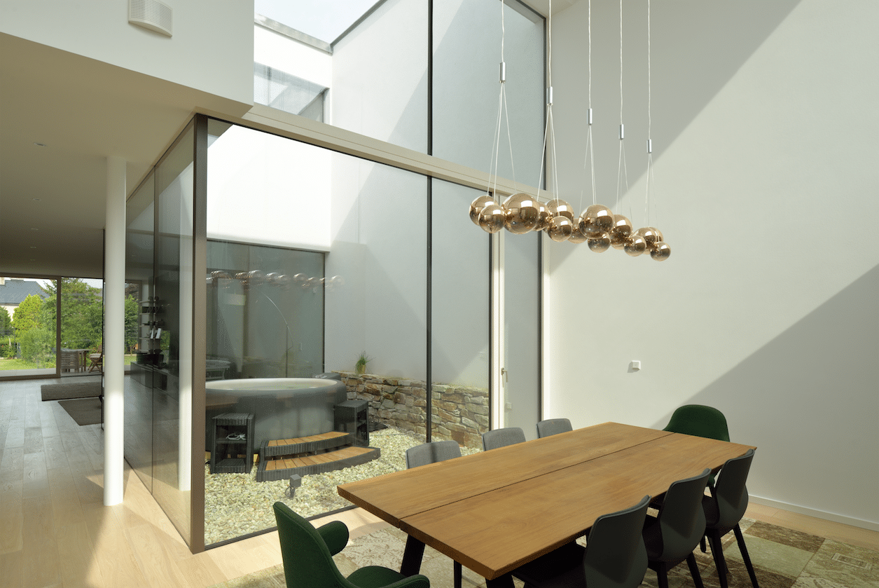 Esszimmer mit schönem Holztisch, moderner Hängeleuchte und mehrstöckiger M SORA Vollverglasung zum Innenhof mit Whirlpool.