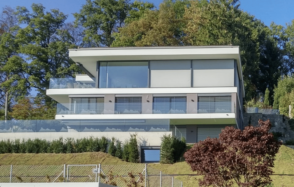 Architektenhaus in Hanglage mit mehreren Balkonen mit Glasgeländern und Fenstern von M SORA.