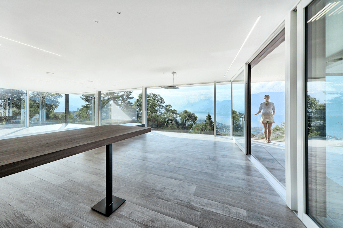 Helles Esszimmer mit deckenhoher Rundumverglasung sowie barrierefreien Schiebetüren zum Balkon hin - ausgestattet mit Glaselementen von M SORA.