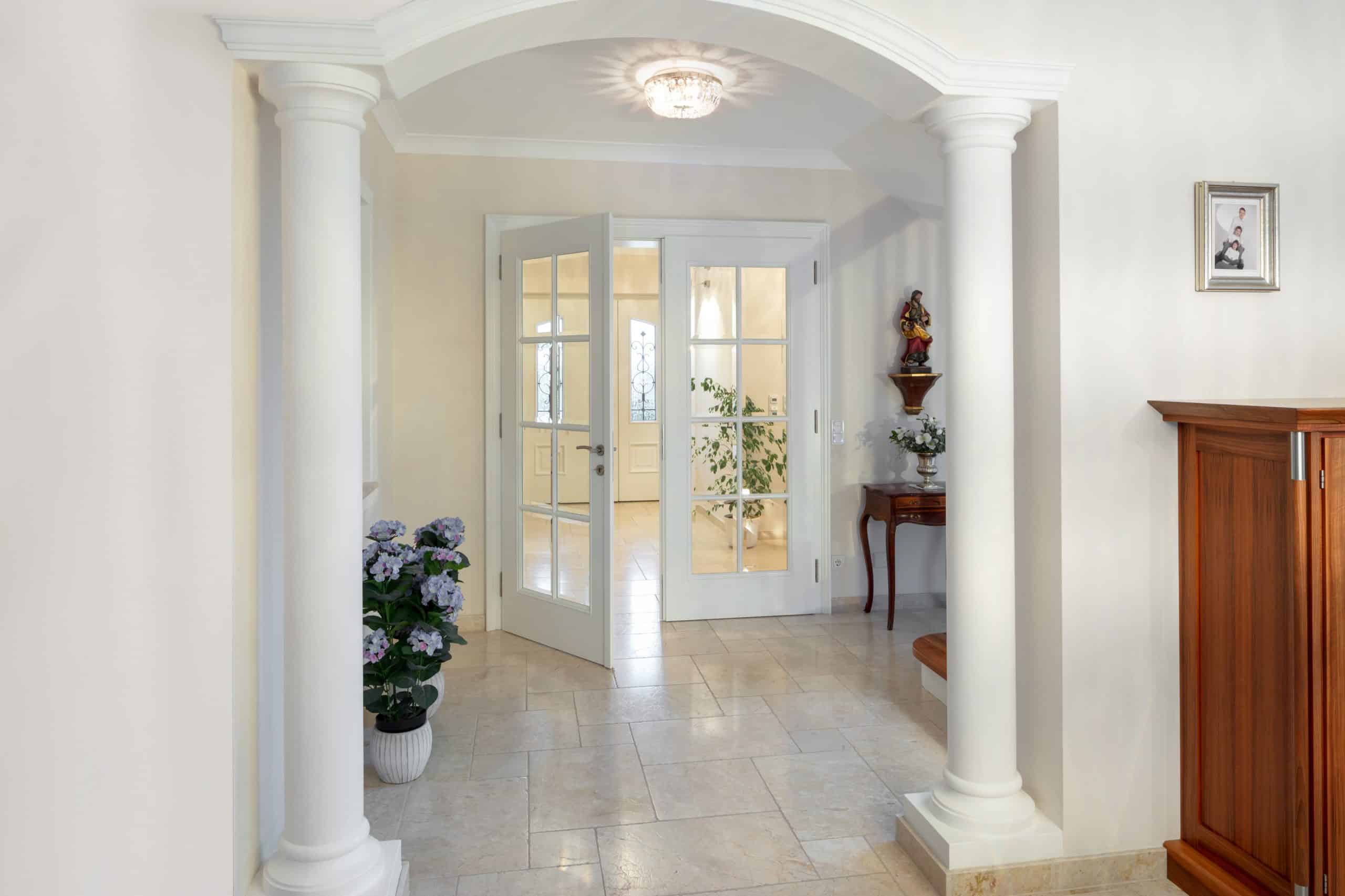 Großzügiger, heller Eingangsbereich mit weißem Marmorboden, Säulen, und einer Doppelflügeltür aus Holz und Glas von Maderböck.
