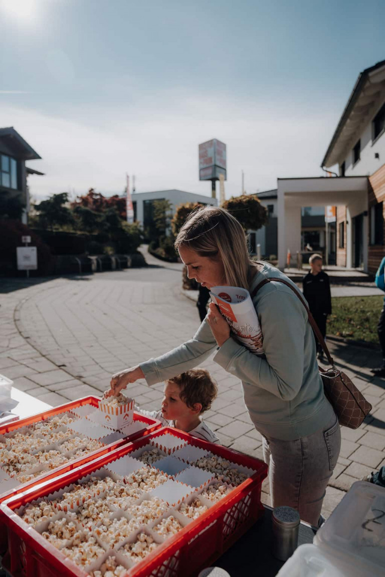 Eine junge Mutter mit kleinem Kind bedienen sich am Popcornstand der Musterhausparkmesse.