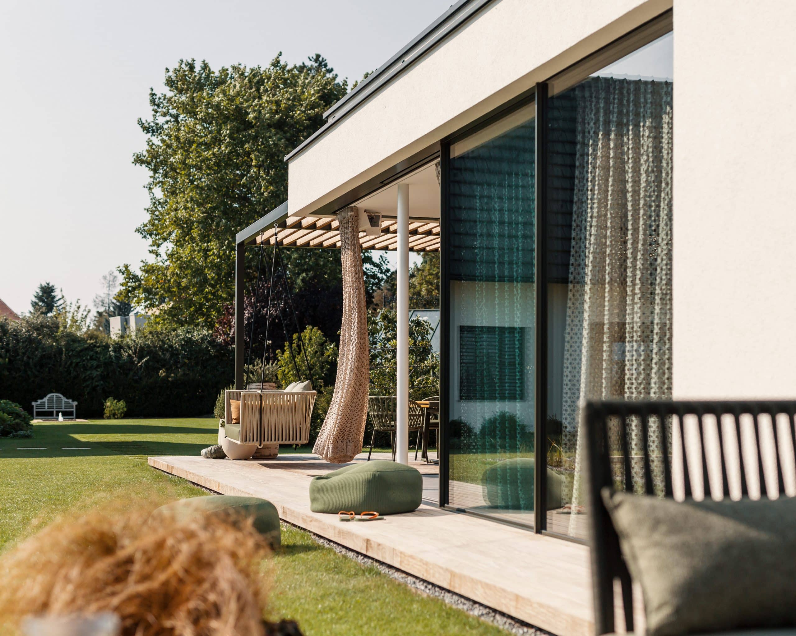 Nentwich zeigt auf diesem Foto die Terrasse eines Hauses, eine Glasfront, einen Hängestuhl aus Holz und moderne Vorhänge.