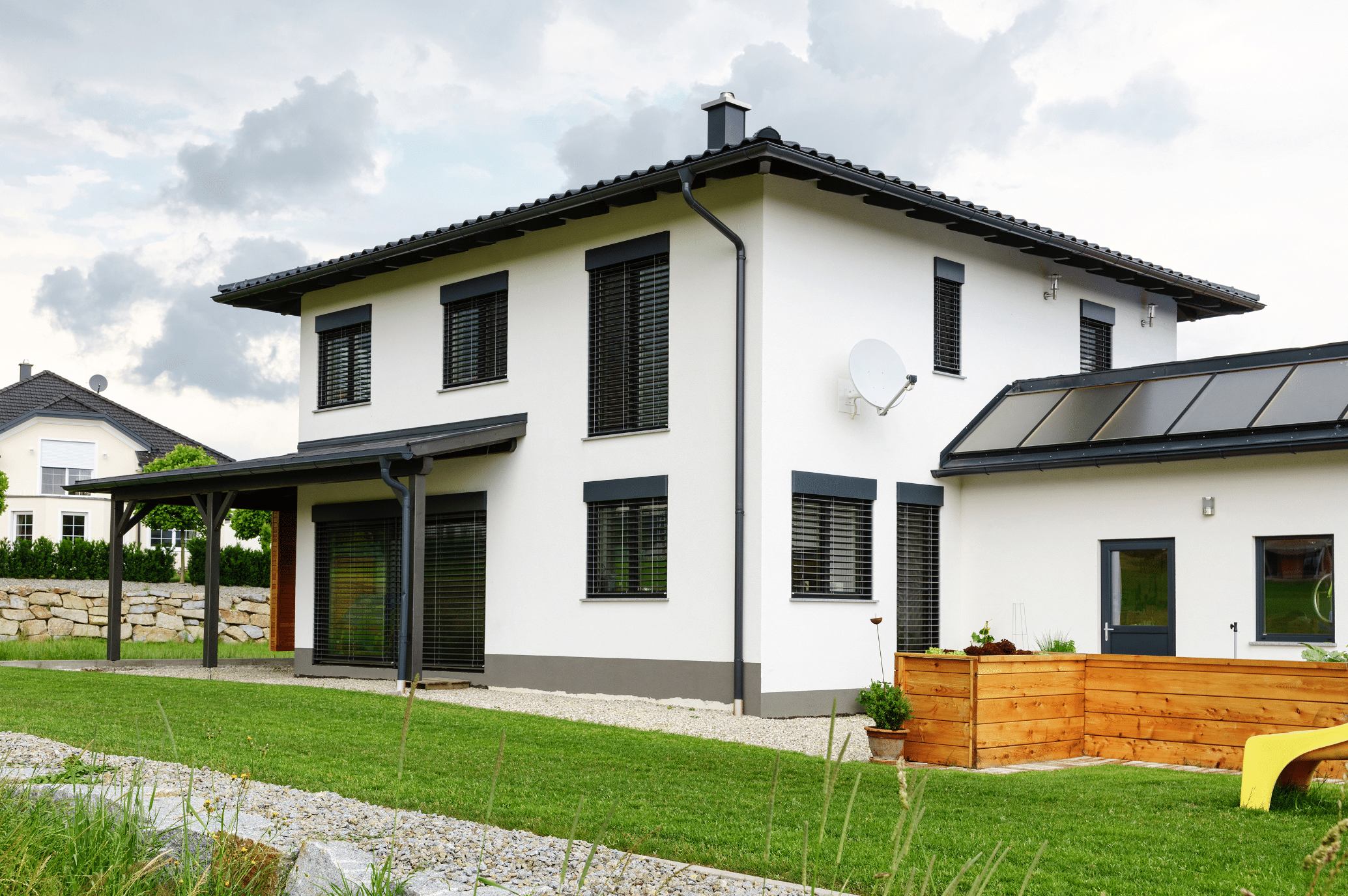 Newo Sonnen- und Insektenschutz zeigt ein weisses Einfamilienhaus mit vielen Fenstern an denen Rollläden als Sonnenschutz montiert sind und eine überdachte Terrasse mit schwarzen Rollläden an den Terrassentüren.