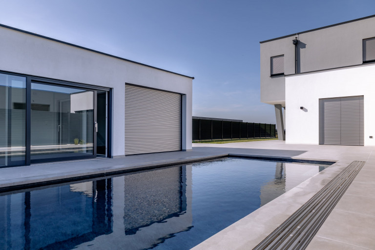 Modernes Flachdach-Wohnhaus mit Terrasse und Pool und zur Gänze geschlossenen silber Jalousien von Newo.