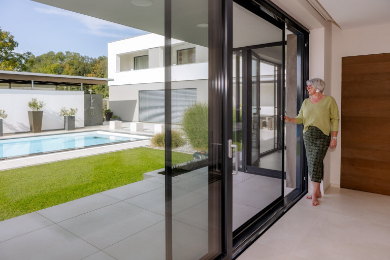 Großflächige Insektenschtutz-Terrassentür zum Schieben mit schwarzem Rahmen von Newo mit Blick auf Terrasse und Pool.