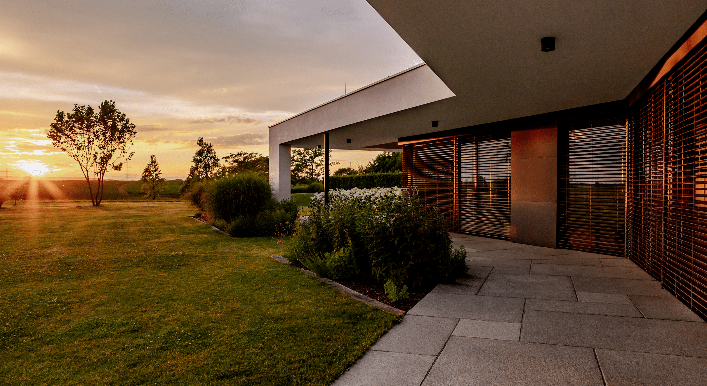 Newo Sonnen- und Insektenschutz zeigt ein modernes Einfamilienhaus mit großen Glasfronten auf denen Rollläden als Sonnenschutz angebracht wurden.