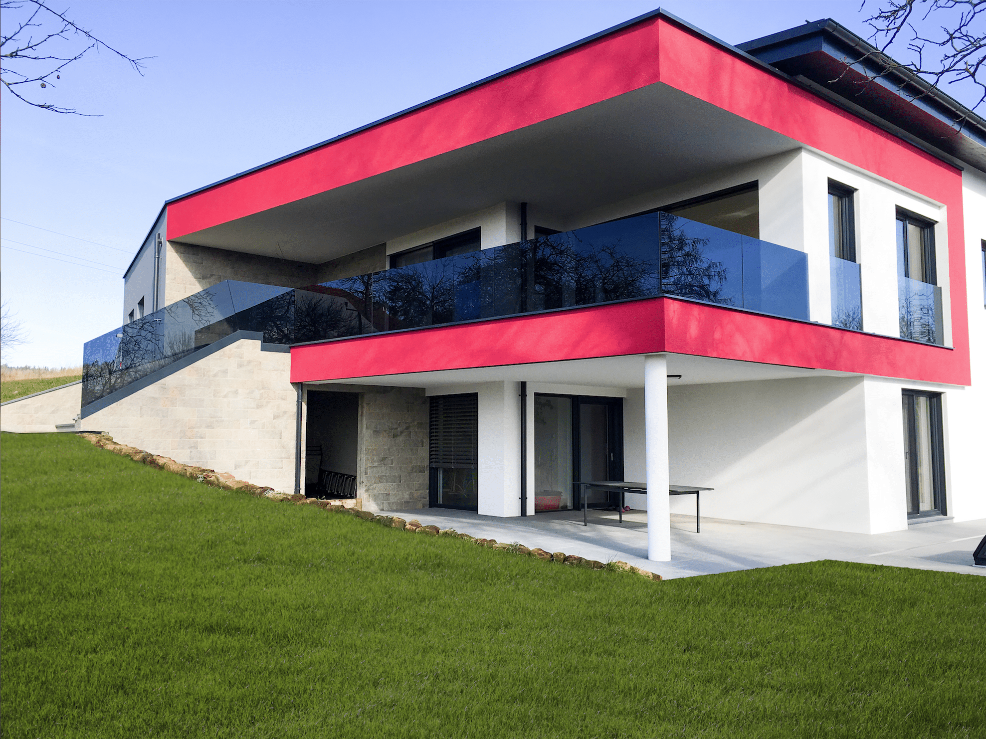 Haus mit teilweise roter Fassade, Terrasse und Balkon mit Glas von Peindl Glasbau.