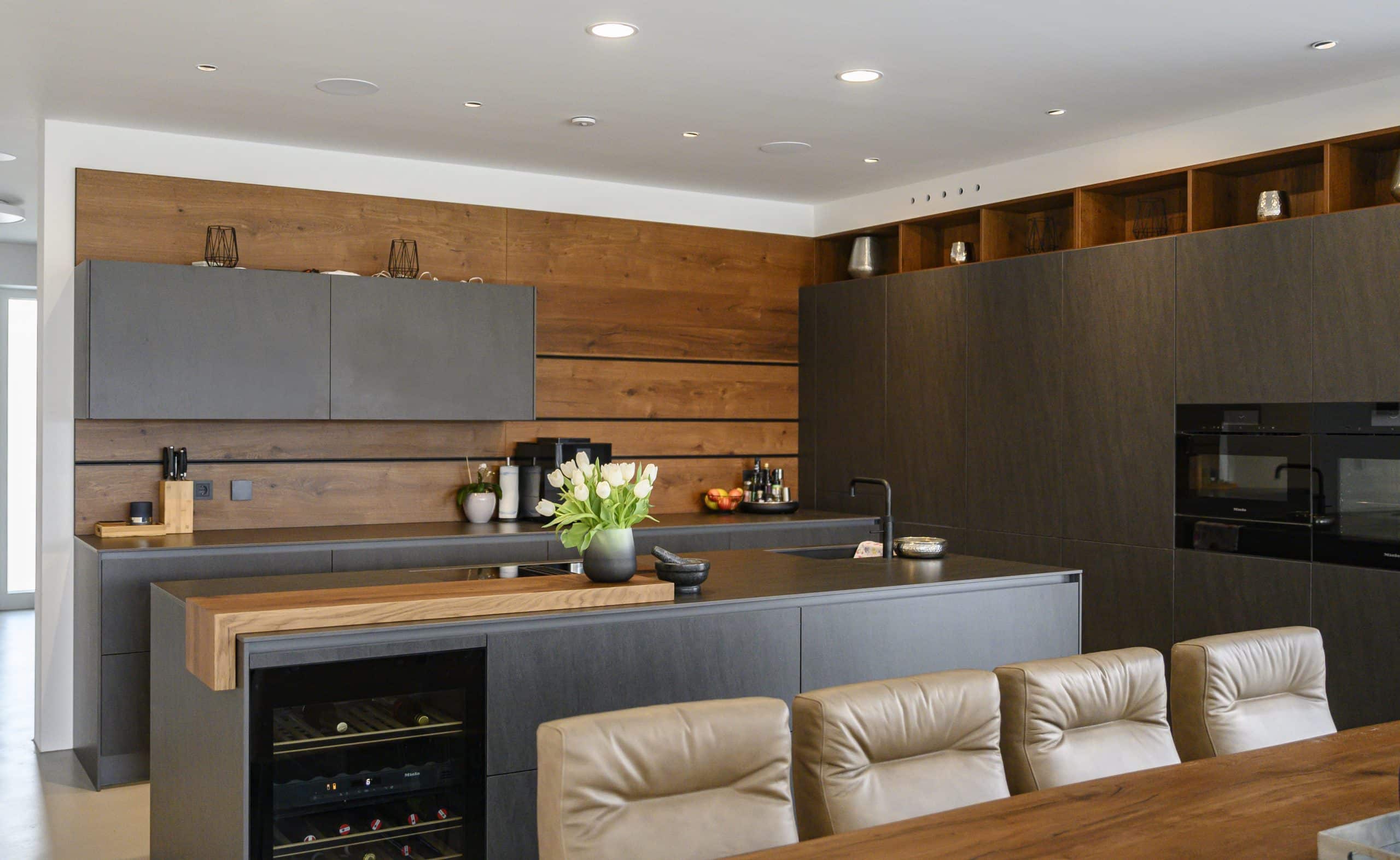reginaplaza präsentiert eine offene Wohnküche mit dunkler Küche, heller Ledergarnitur und ästhetischen Dekoelementen.