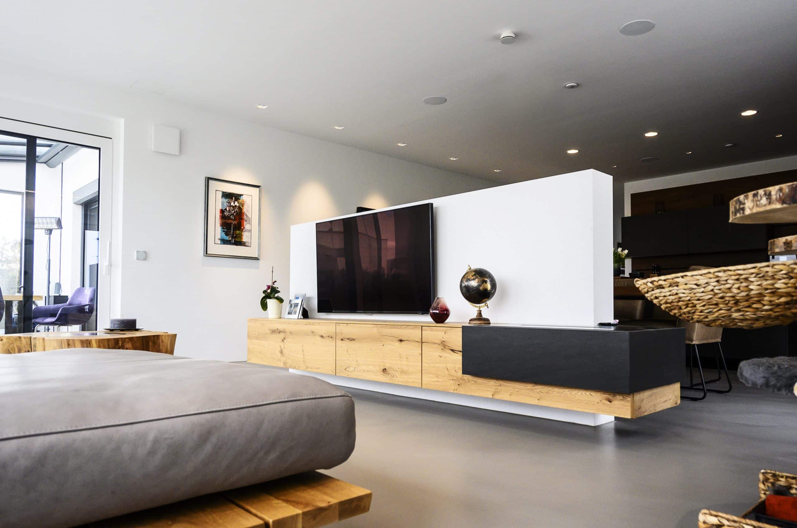 reginaplaza präsentiert ein helles, sehr modernes Wohnzimmer mit Zugang zum Balkon und einem Fernseher hängend auf der Wohnwand aus Holz.