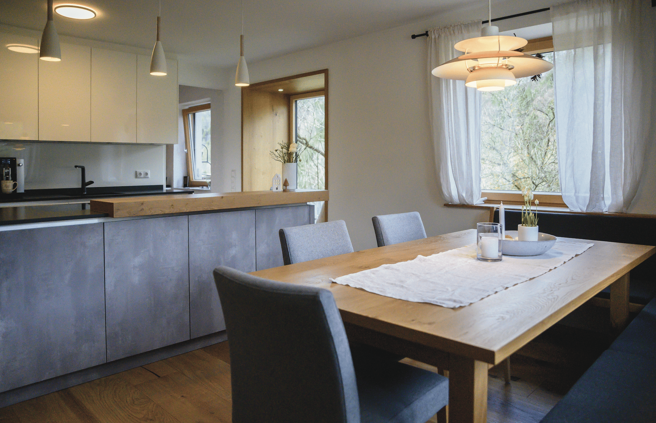reginaplaza zeigt eine Küche mit grauem Küchenblock, einer schwarzen Arbeitsplatte und den Essbereich mit einem Holztisch und grauen Stühlen. © Thomas Gobauer