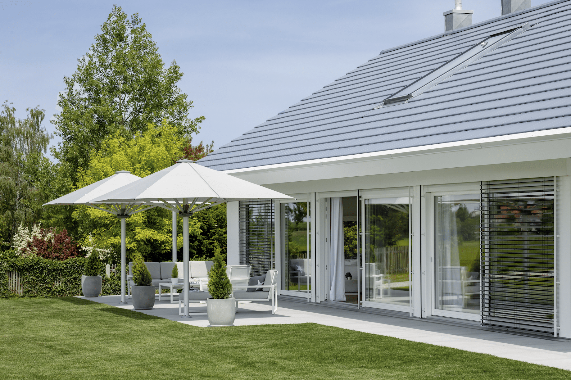 Haus "Poering" von Regnauer mit Terrasse mit Gartenmöbel und aufgespannten Sonnenschirmen.