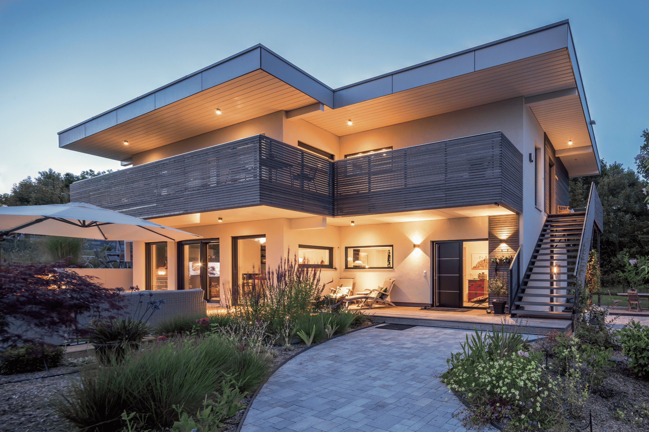 Regnauer Fertighaus zeigt ein modernes Einfamilienhaus mit Holzverkleidung und schöner Beleuchtung in der Abenddämmerung.