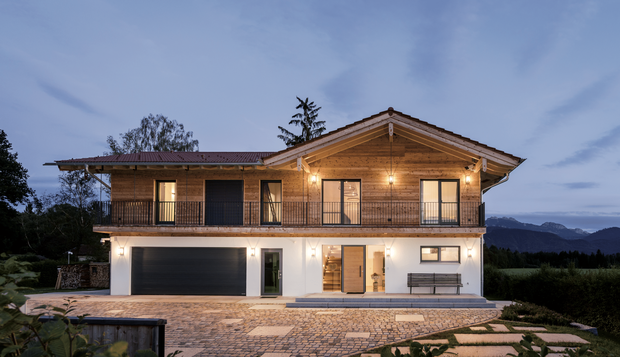 Regnauer zeigt ein Einfamilienhaus mit heller Holzverkleidung und einer Doppelgarage mit dunklem Garagentor und einen Balkon mit Metallgeländer.